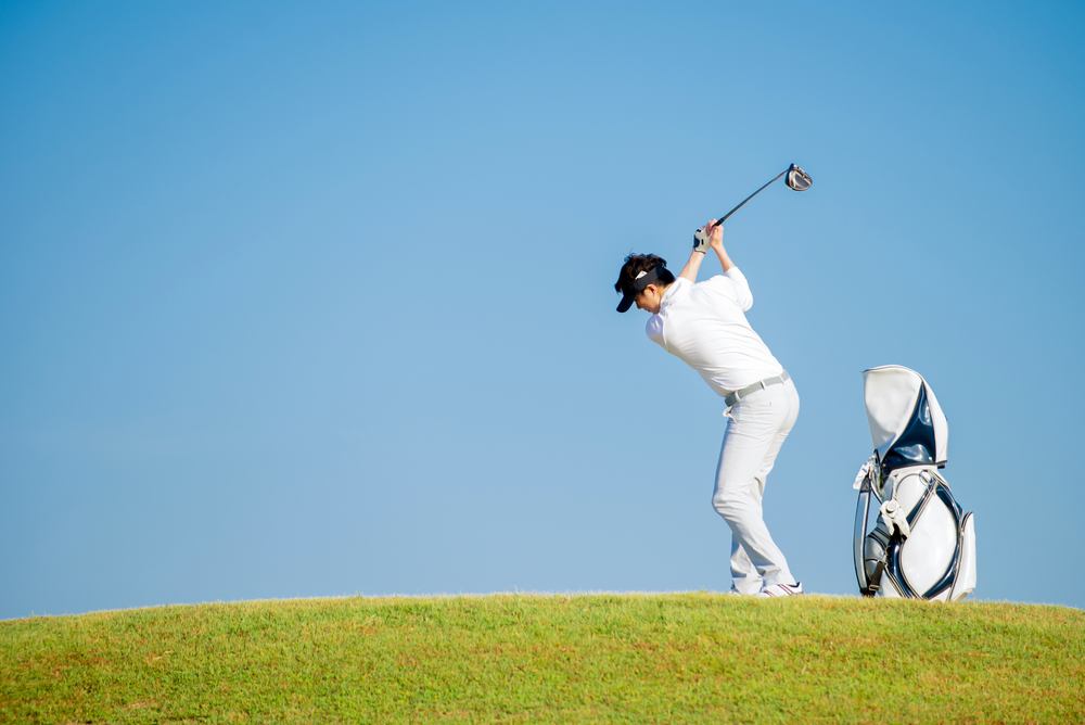 Asian,Man,Golfer,Standing,On,Slope,With,Golf,Bag,Hitting